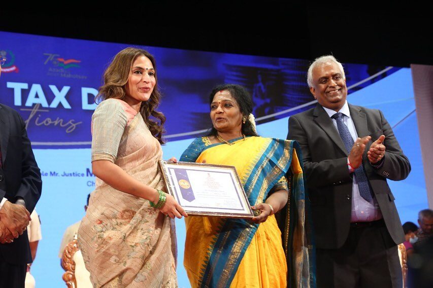 Aishwarya Rajinikanth on stage at a public ceremony, presenting a certificate to a recipient