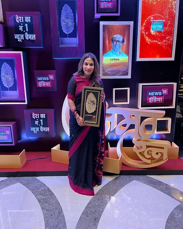 Aishwarya Rajinikanth on stage in a dark saree, holding a framed award