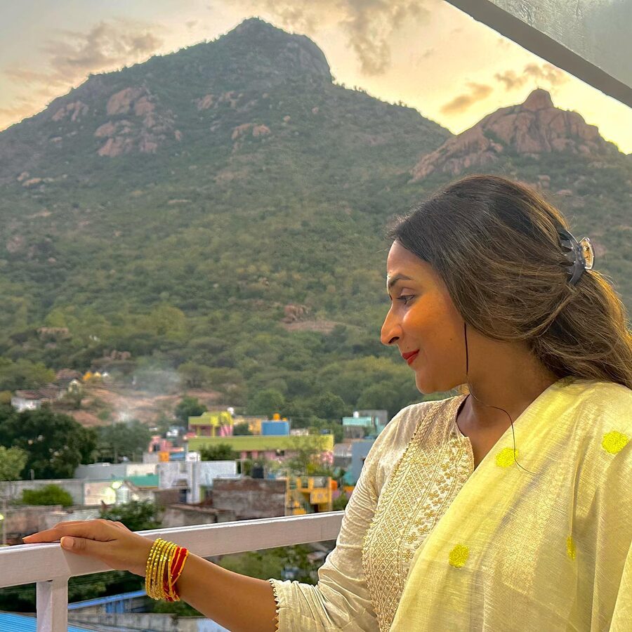 Aishwarya Rajinikanth in a pale yellow outfit on a balcony, looking out towards a hillside at sunrise
