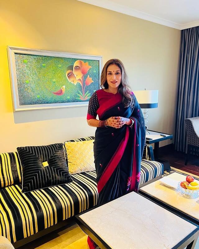 Aishwarya Rajinikanth standing in a deep blue and maroon saree beside a framed artwork