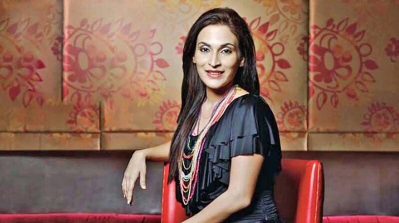 Aishwarya Rajinikanth seated against a patterned backdrop in a dark top